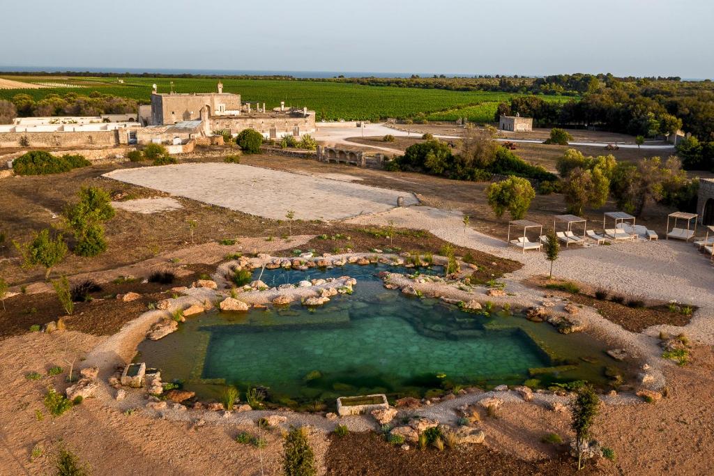 Aerial view of a Puglian masseria with a natural stone swimming pond surrounded by olive groves and vineyards